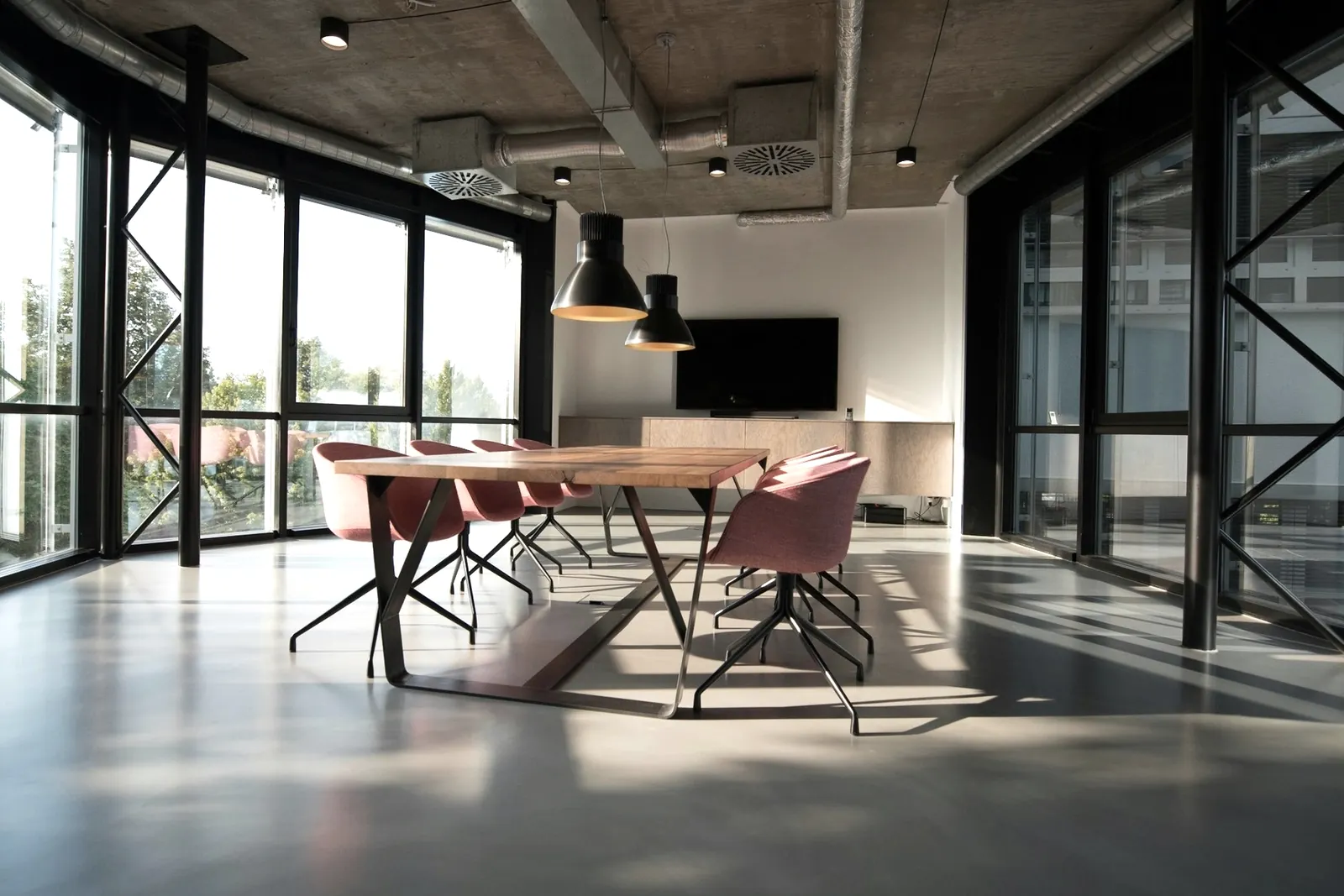 Salle de réunion vitrée, table en bois et chaises, traversée par la lumière naturelle.